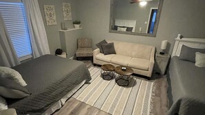 Un dormitorio con dos camas individuales, un sofá, un ventilador de techo, un espejo y una alfombra estampada.