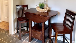 Un comedor con una mesa de madera oscura, dos sillas y un espejo decorativo en la pared.