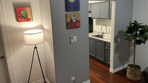 Un couloir avec une lampe, des œuvres d’art, une plante en pot et un coin cuisine avec des placards et un évier.