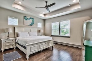Une chambre à coucher avec un lit, des tables de chevet, un ventilateur de plafond et une fenêtre avec des stores.