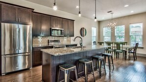 Uma cozinha moderna com eletrodomésticos de aço inoxidável, uma ilha grande com banquetas e uma área de refeições com vista para o exterior.