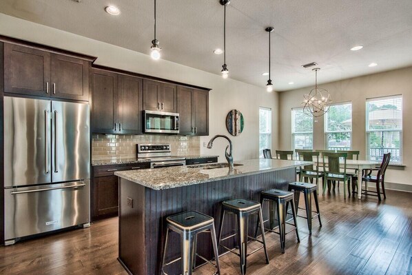 A modern kitchen with stainless steel appliances, a large island with bar stools, and a dining area with a view of the outdoors.