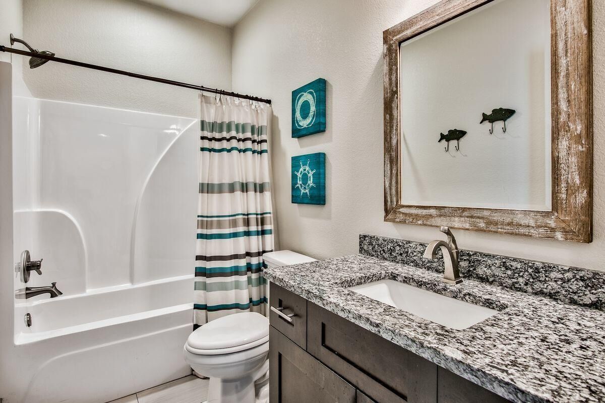A bathroom with a bathtub, toilet, and a granite countertop sink.