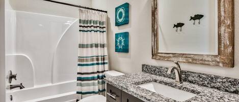 A bathroom with a bathtub, toilet, and a granite countertop sink.