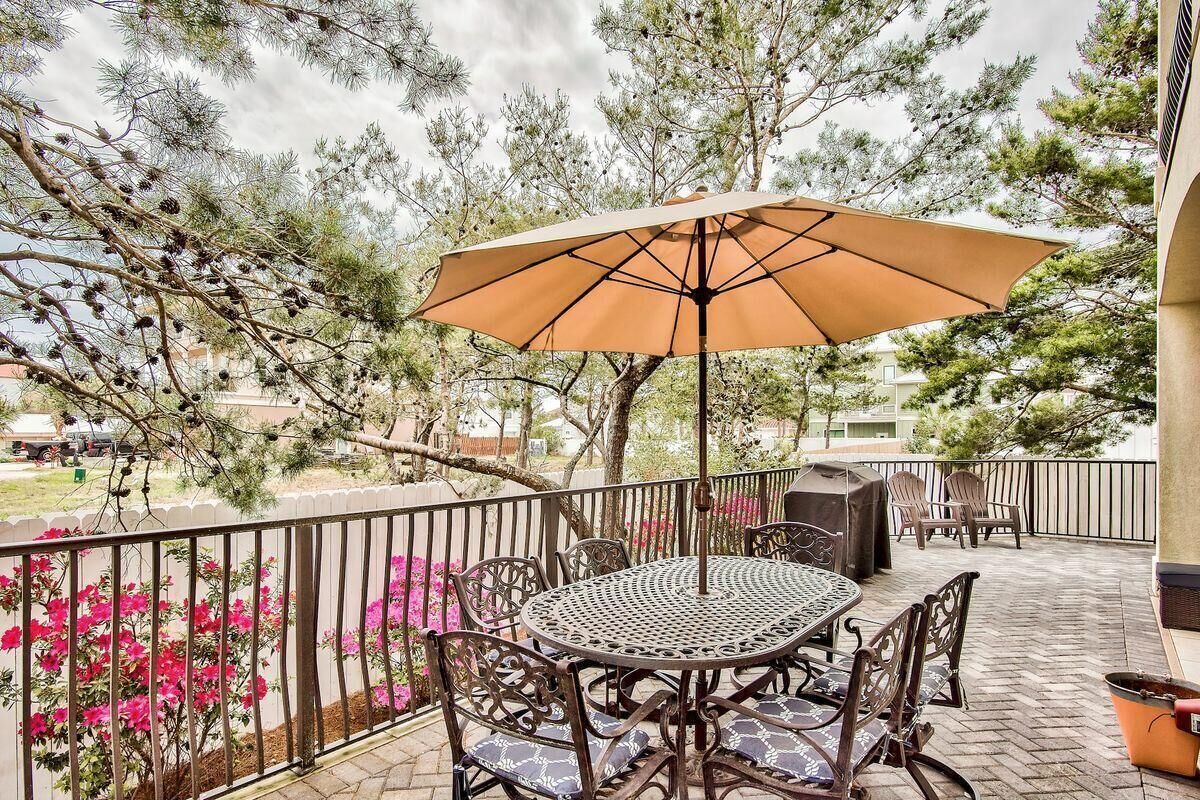 Une terrasse extérieure avec une table ronde et des chaises, un grand parasol et une vue sur les arbres et les fleurs.