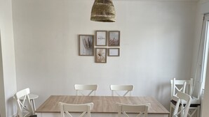 Ein Essbereich mit einem Holztisch, weißen Stühlen, einer Hängeleuchte und gerahmten Bildern an der Wand.