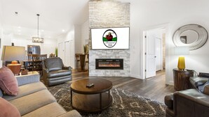 Ein modernes Wohnzimmer mit Kamin, Ledersofas, einem Essbereich und einer Küche im Hintergrund.