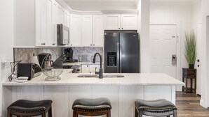 Eine moderne Küche mit weißen Schränken, Edelstahlgeräten, einer großen Kochinsel mit Barhocker und einem Deckenventilator.