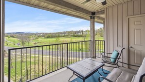 Ein Balkon mit Tisch und Stühlen, einem Deckenventilator und Blick auf einen Golfplatz sowie Wohngebiet.