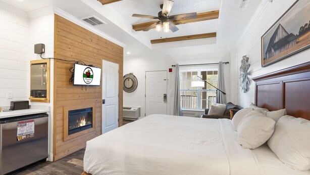 A modern hotel room with a bed, a fireplace, a ceiling fan, and a view of the outdoors. - Queen Suite Near Hwy 76 • Close to Shows • Sleeps 2 (Branson)