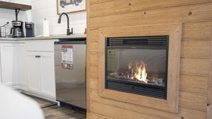 A modern kitchen with white cabinets, a built-in dishwasher, and a wood-paneled fireplace with a visible fire. - Queen Suite Near Hwy 76 • Close to Shows • Sleeps 2 (Branson)