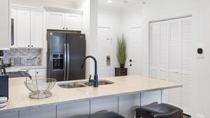 A modern kitchen with white cabinetry, a stainless steel refrigerator, a granite countertop, and a black faucet.