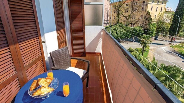 A balcony with a table set for breakfast, a chair, and a view of the street and buildings.