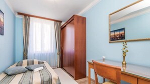 A bedroom with a bed, a desk, a chair, a mirror, and a window with curtains.