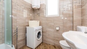 A compact bathroom with a washing machine, toilet, and a glass shower enclosure.