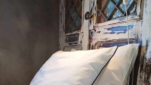 A bed with a white pillow and a white blanket in a room with a rustic wooden door and a window with decorative tiles. - Ruby Charm Houses 9 116352/AL (Porto)