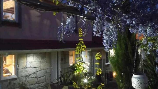 A house with a stone facade, a porch with potted plants, and a hanging light fixture. - Ruby Charm Houses 9 116352/AL (Porto)