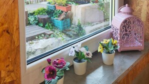A window with a view of a garden, a pink lantern, and several potted plants on a windowsill. - Ruby Charm Houses 9 116352/AL (Porto)
