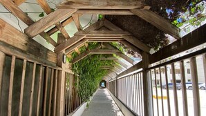 A covered pedestrian walkway with wooden beams and metal railings, leading to a distant view.