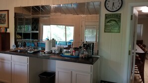 Cozinha com uma ilha grande, pia e máquina de café. Há armários, uma lixeira e um relógio na parede.