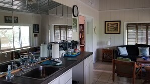 Uma cozinha com um espelho grande, pia de aço inoxidável e um espaço de refeições com sofá preto e cadeiras de vime.