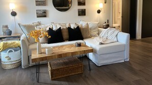A modern living room with a white sofa, a wooden coffee table, and a large mirror on the wall. - Beautiful ski in-ski out condo at Okemo Mountain (Ludlow)
