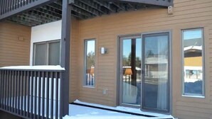 A building with a balcony, large sliding glass doors, and a snow-covered ground. - Beautiful ski in-ski out condo at Okemo Mountain (Ludlow)