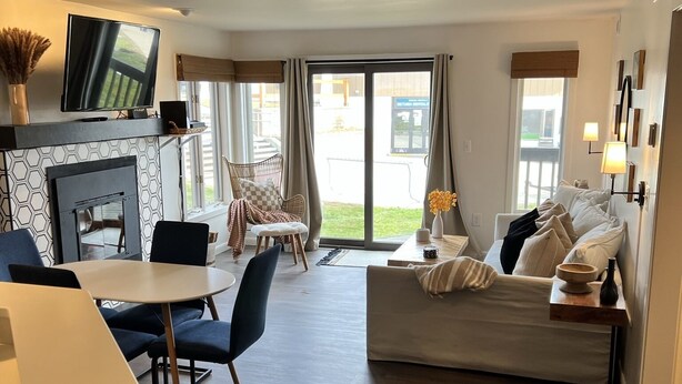 A modern living room with a sofa, a dining table, and a TV mounted on the wall. - Beautiful ski in-ski out condo at Okemo Mountain (Ludlow)