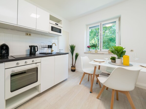 A modern kitchen with white cabinets, a built-in oven, and a dining area with a table and chairs. - EG L -schöne 70m² 2-zimmer City Wohnung im Zentrum (Freilassing)