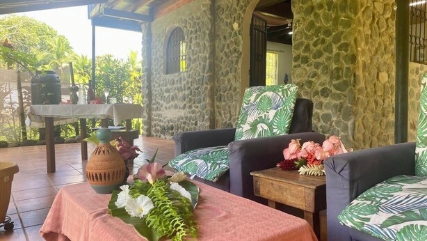 A stone-walled room with a covered patio, furnished with two sofas and a table, decorated with flowers and a vase. - Tranquil apartment near beach front  (Playa Zancudo)