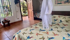 A bedroom with a bed featuring a bird pattern, a standing fan, a bedside table with a flower, and a door leading to a balcony. - Tranquil apartment near beach front  (Playa Zancudo)