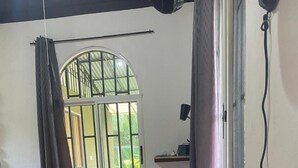 A small room with a bed, a desk, a window with curtains, and a small table with a flower vase. - Tranquil apartment near beach front  (Playa Zancudo)
