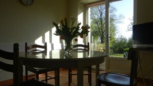 Un comedor con mesa de vidrio, sillas y un florero con flores.