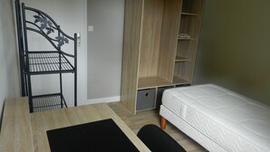 Una habitación compacta con cama, un escritorio y silla, y un armario empotrado con estantes.