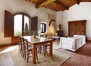 Uma sala de estar ampla com uma mesa de jantar de madeira, sofá branco e uma grande janela com vista.