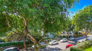 A residential area with a tree-lined street, parked cars, and a swimming pool.