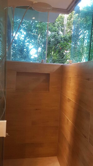 A shower area with wooden tiles and a window overlooking greenery.