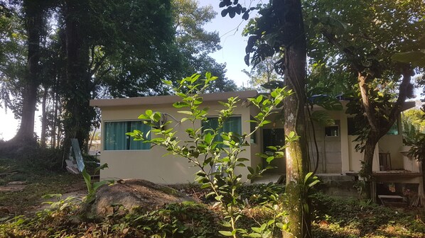 A small, single-story building with a flat roof, surrounded by dense foliage and trees.
