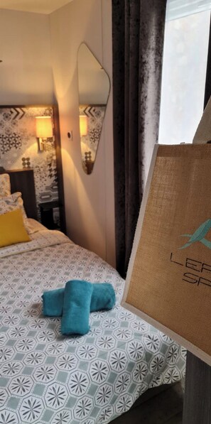 A hotel room with a patterned bedspread, a mirror, a nightstand with a lamp, and a towel on the bed. - Luxury Bungalow/Mobile Home with Ocean View on the Ile d'Or, Saint-Raphaël—Accommodates 4 People (Saint-Raphaël)