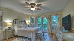 A bedroom with a bed, wooden floor, ceiling fan, and a television on a dresser.