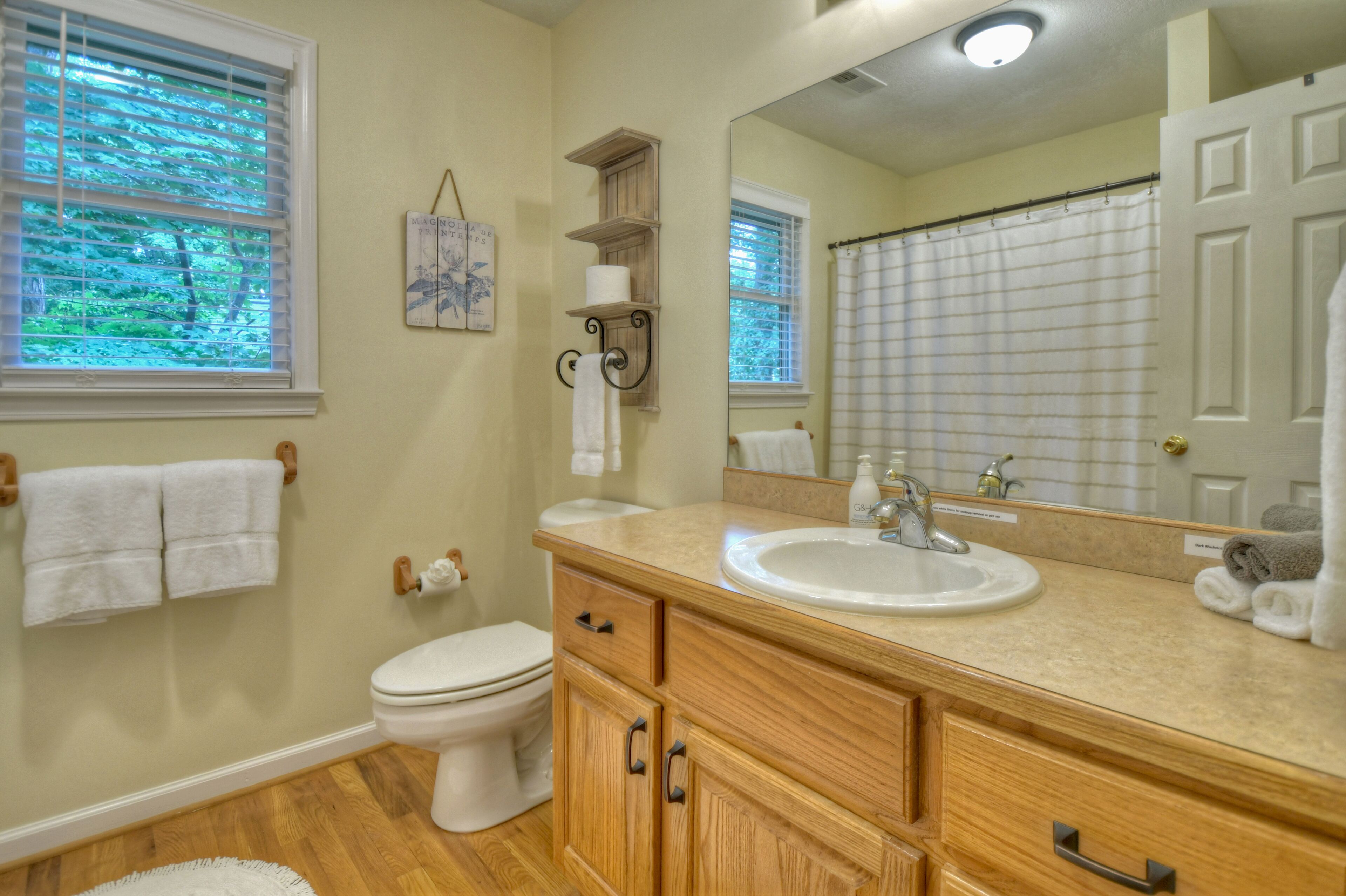 A bathroom with a toilet, sink, wooden vanity, towel rack, and a large mirror.