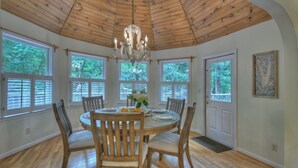 A dining room with a wooden ceiling, large windows, and a chandelier.