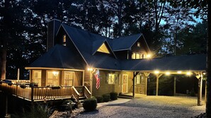 A two-story wooden house with a porch, a gravel driveway, and an American flag.