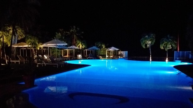A nighttime swimming pool with lounge chairs and umbrellas.