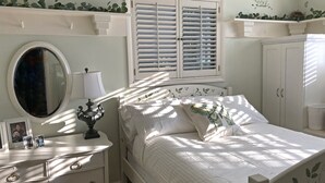 Un dormitorio con cama, mesita de noche, cómoda, espejo, ventana con contraventanas y armario.