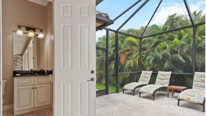 A room with a large glass door leading to a tropical garden view, a kitchen with light-colored cabinets, and two lounge chairs with patterned cushions. - 5 min walk to the beach, perfect pool, bbq, spa, beautiful home (Marco Island)