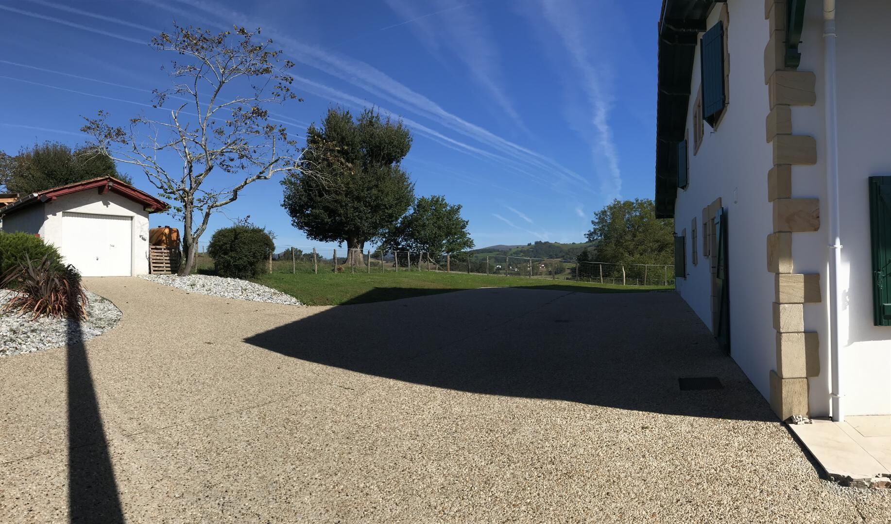A residential property with a gravel driveway, a garage, and a white building with green shutters.