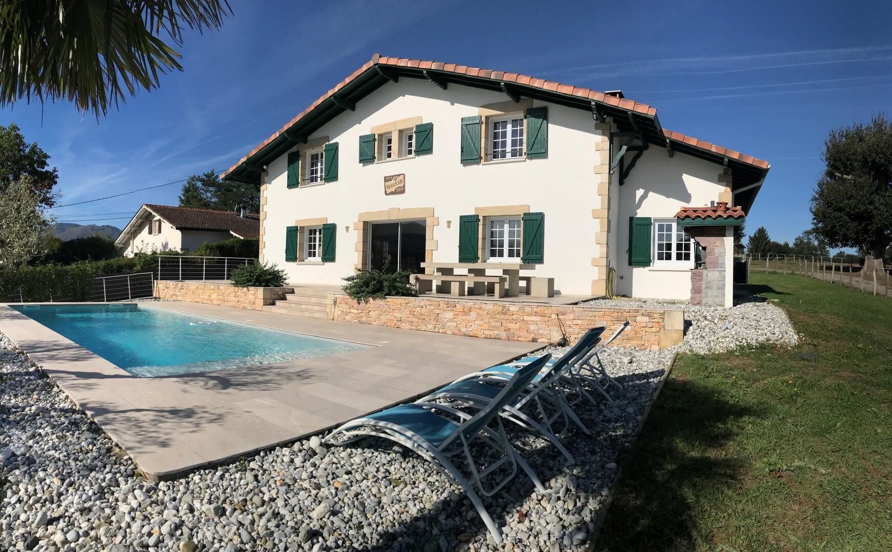 Ein zweistöckiges Haus mit Swimmingpool, Steinmauern und grünen Fensterläden.