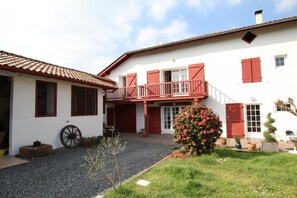 A two-story building with a balcony, a garage, and a garden with flowers.