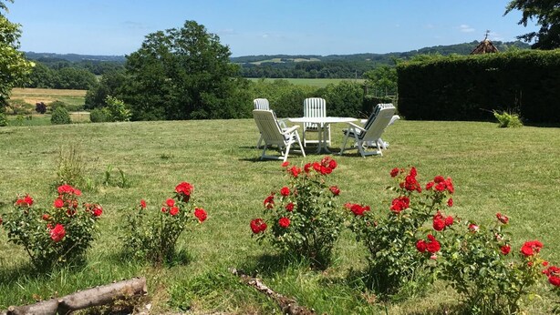 A grassy outdoor area with a table and chairs, surrounded by red flowers and trees. - Bernet - Labastide-villefranche (LABASTIDE-VILLEFRANCHE)